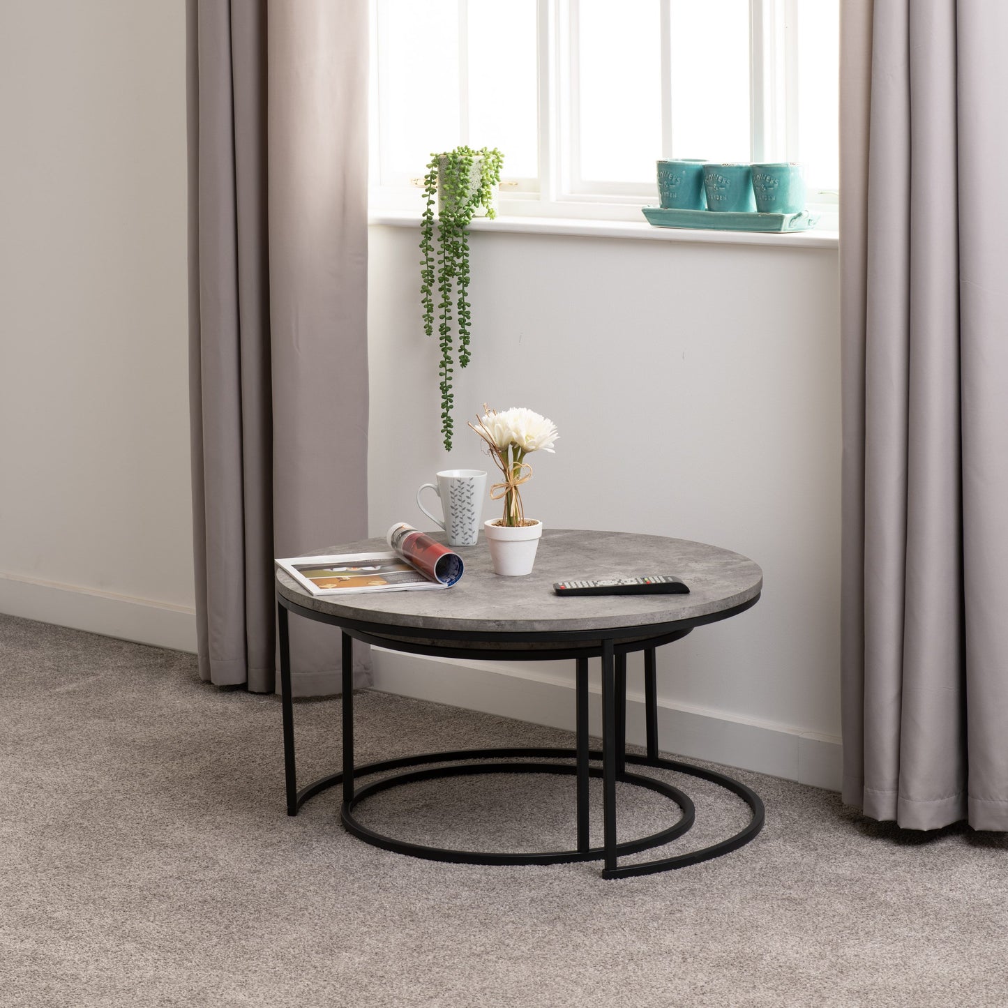 Round coffee table with decorative items in a room with curtains and a window.