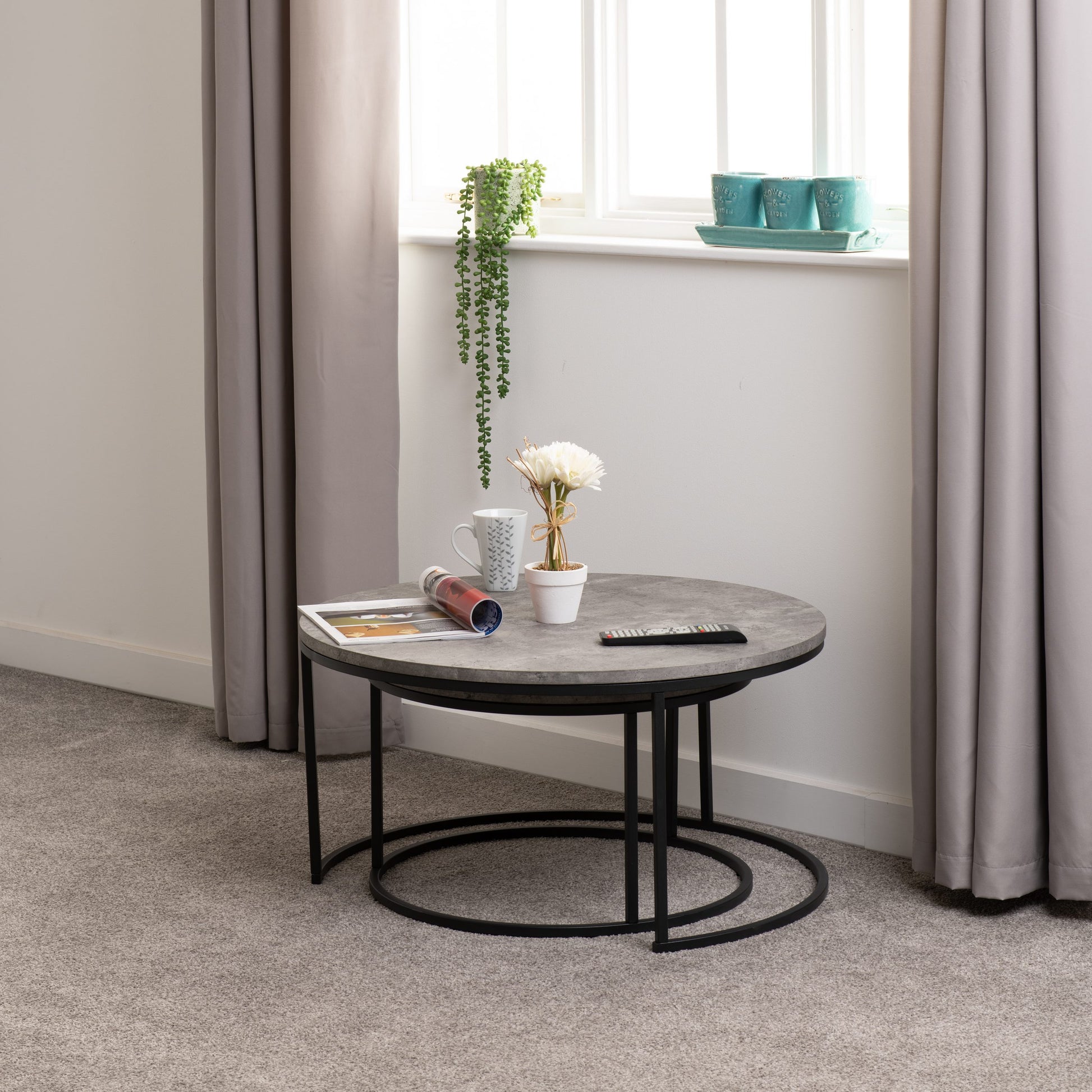 Round coffee table with decorative items in a room with curtains and a window.