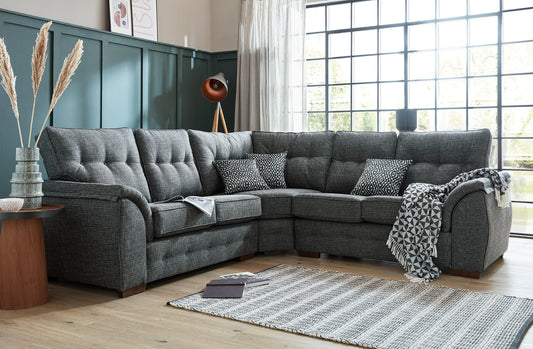 A large gray fabric corner sofa with multiple cushions, placed in a room with a striped rug and a blue wall in the background.