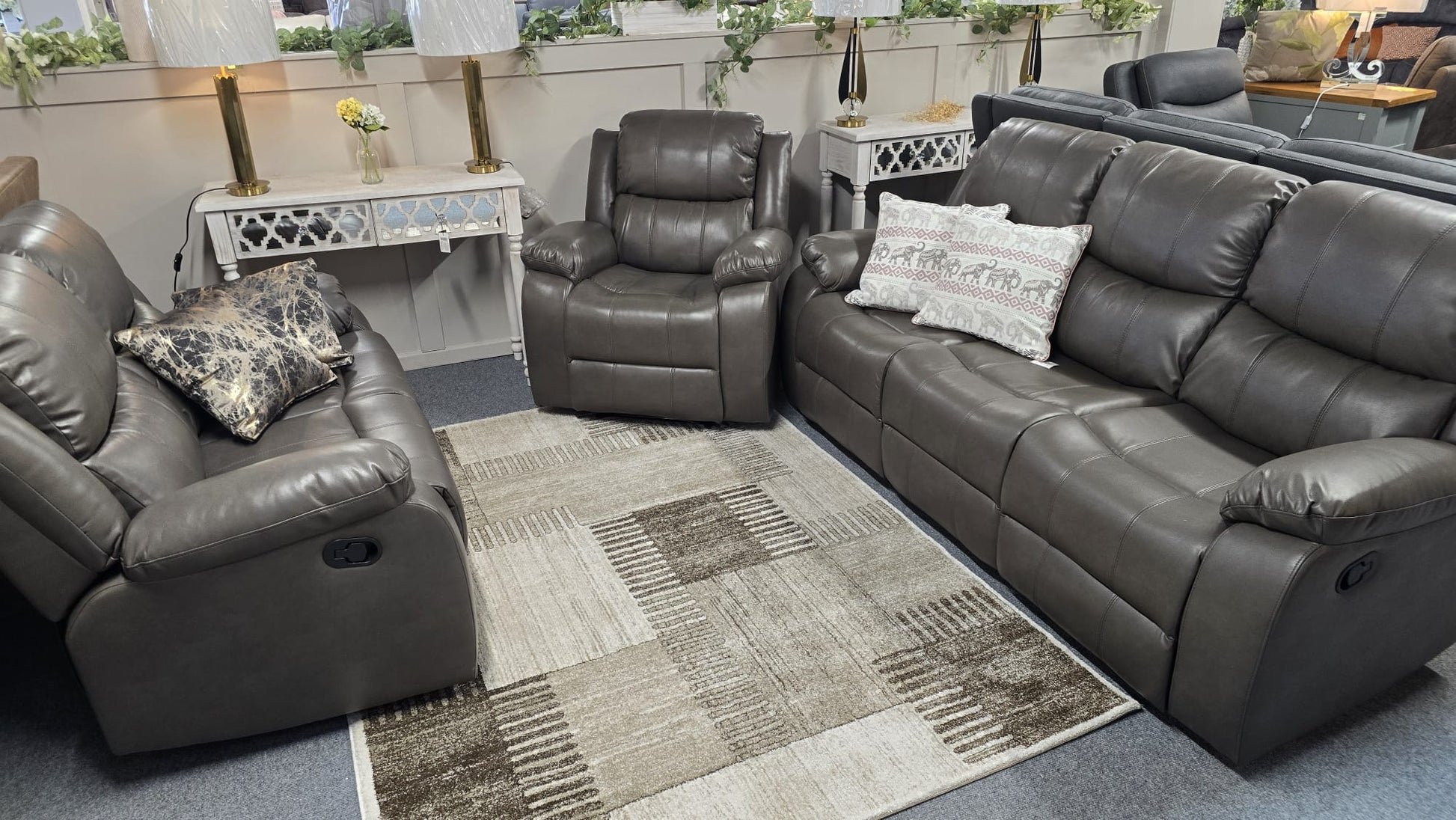 Gray leather reclining sofa set in a living room setting with decorative pillows and a rug.