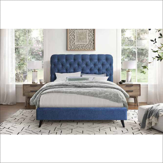 Blue upholstered bed in a bedroom setting with white walls and large windows.