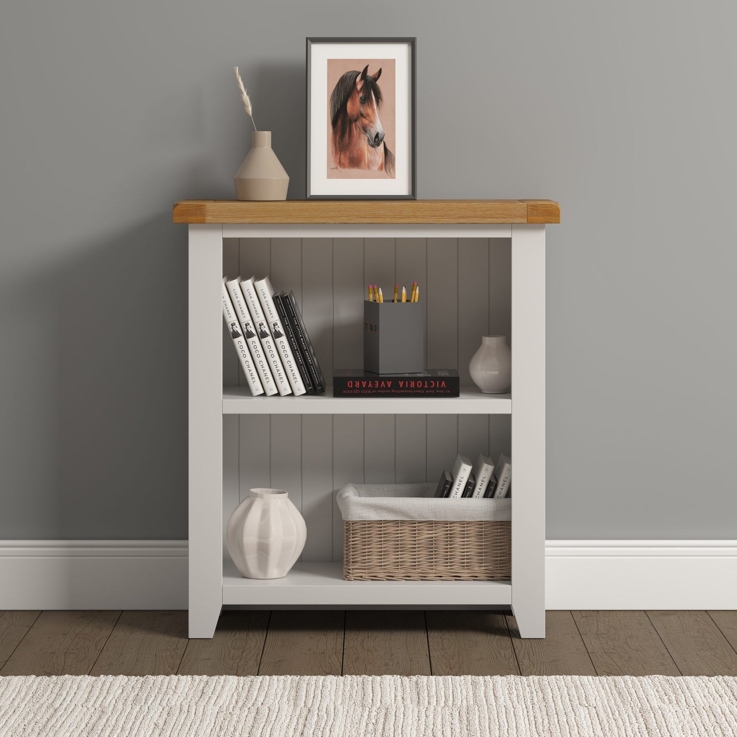 White bookshelf with wooden top against a gray wall, displaying books, a basket, and decorative items.
