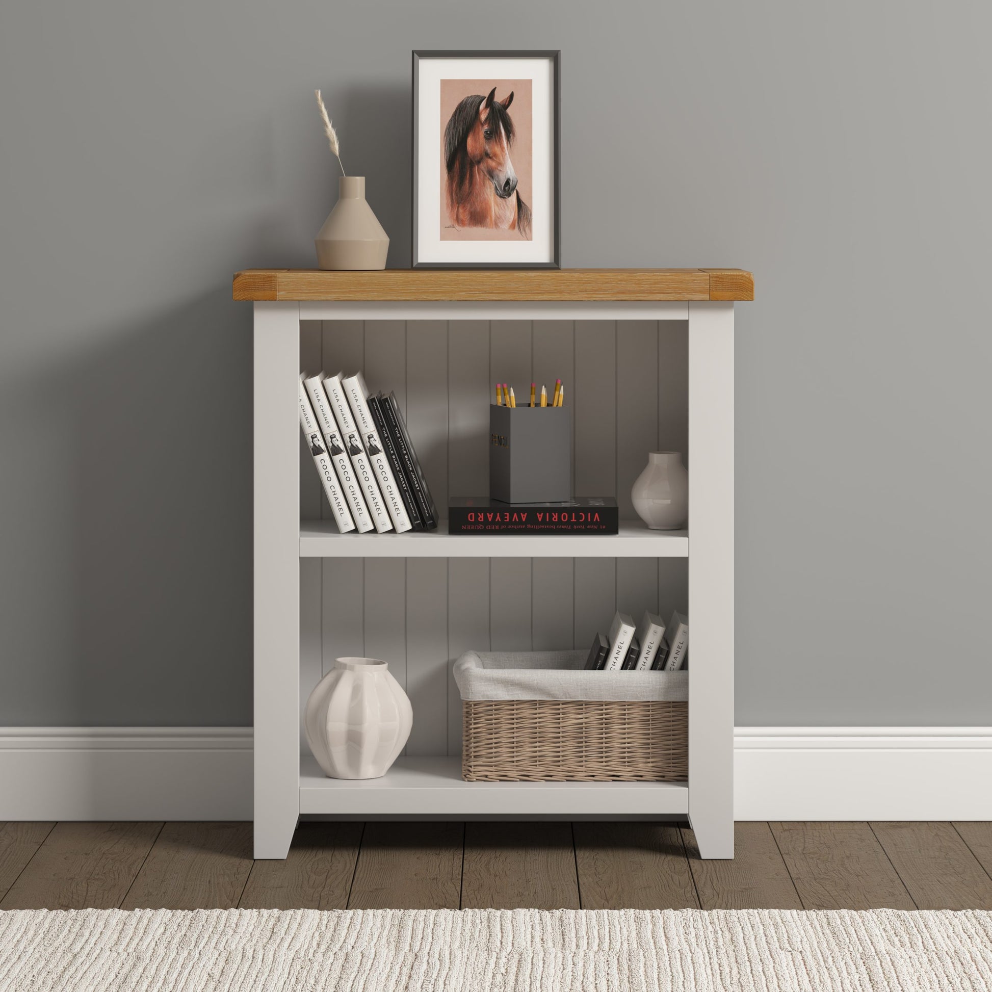 White bookshelf with wooden top against a gray wall, displaying books, a basket, and decorative items.