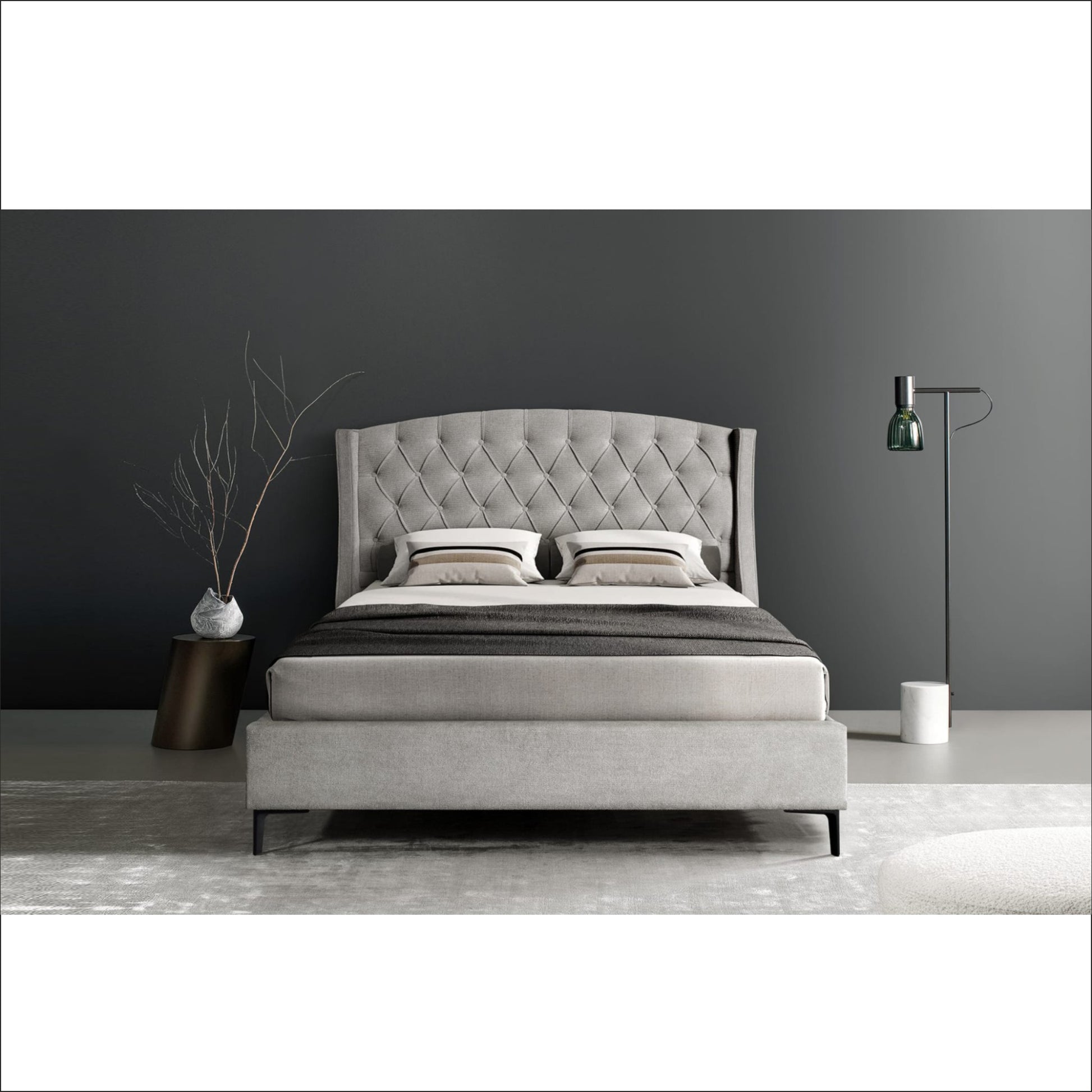 Gray upholstered bed in a minimalistic bedroom with dark walls and a lamp.