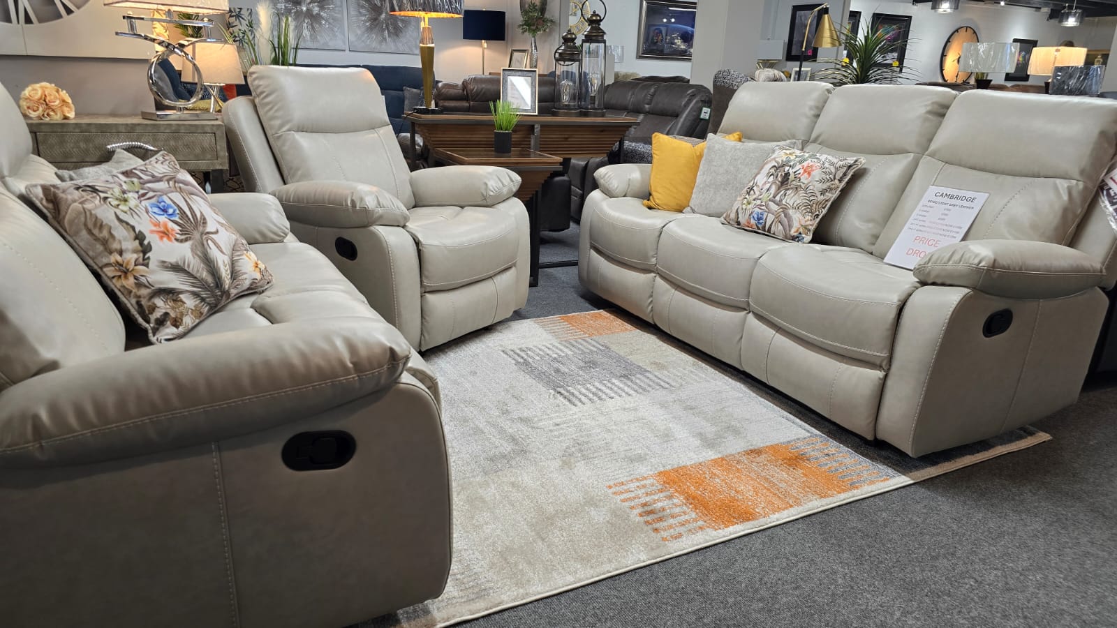 Light Beige leather recliner sofa set in a showroom with decorative pillows and a rug.