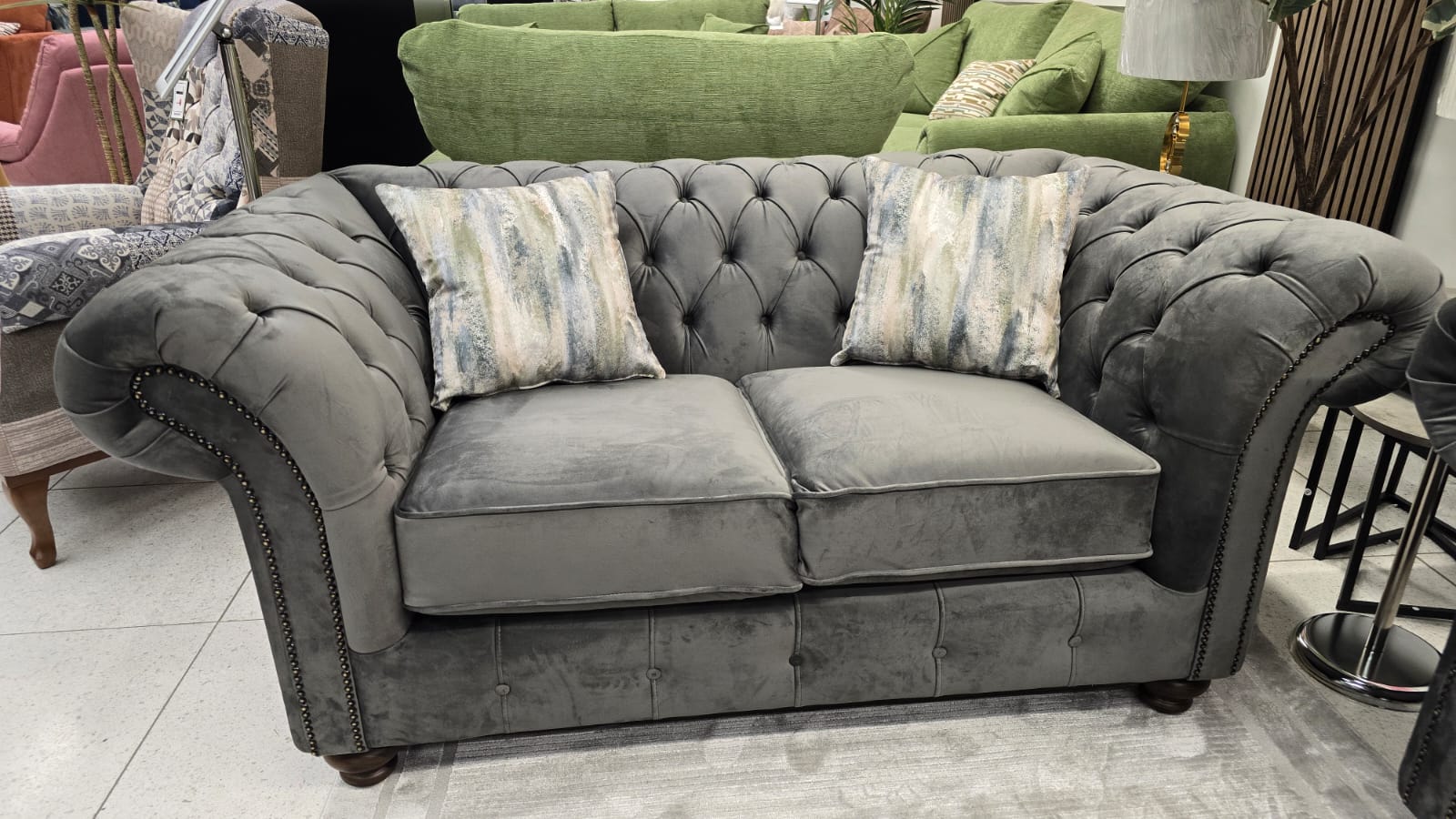 Gray tufted sofa with patterned cushions in a furniture store setting